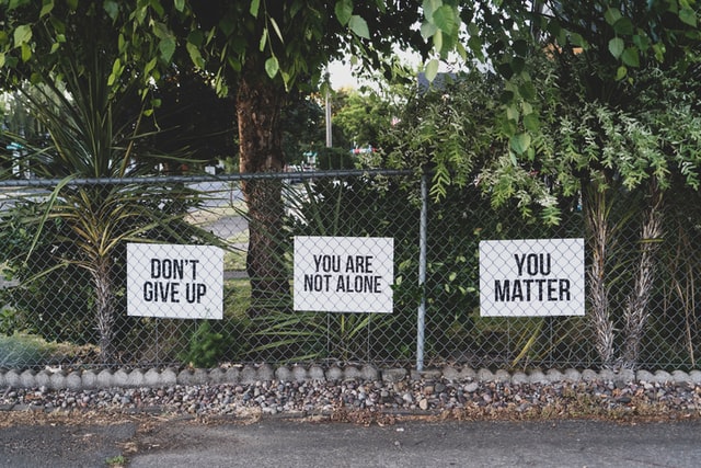 three signs on fence stating "dont give up" "you are not alone" "you matter"