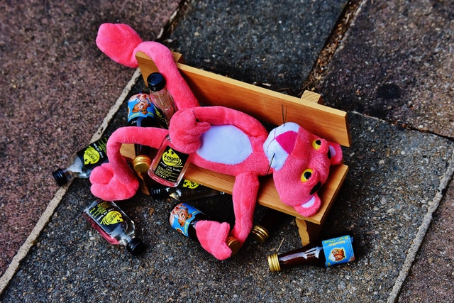 pink panther lying on street bench surrounded by alcohol bottles